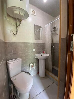 Une salle de bain Ă©quipĂ©e de toilettes, dâun lavabo, dâune douche et dâun miroir.