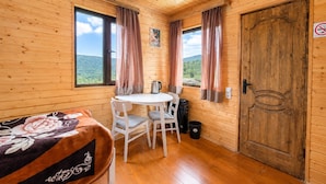 Habitación de cabaña de madera con una cama, una mesa redonda, dos sillas, una tetera y una puerta con un cartel de no fumar.