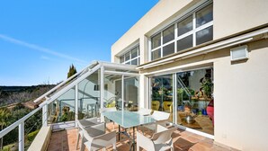Una casa moderna con balcón de vidrio, muebles blancos y vista del paisaje circundante.