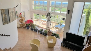 Amplia sala de estar con televisor grande, asientos cómodos, una mesa de comedor y vistas al exterior.