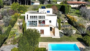 Una casa moderna de dos pisos con un amplio ventanal, piscina y un jardín cuidado.