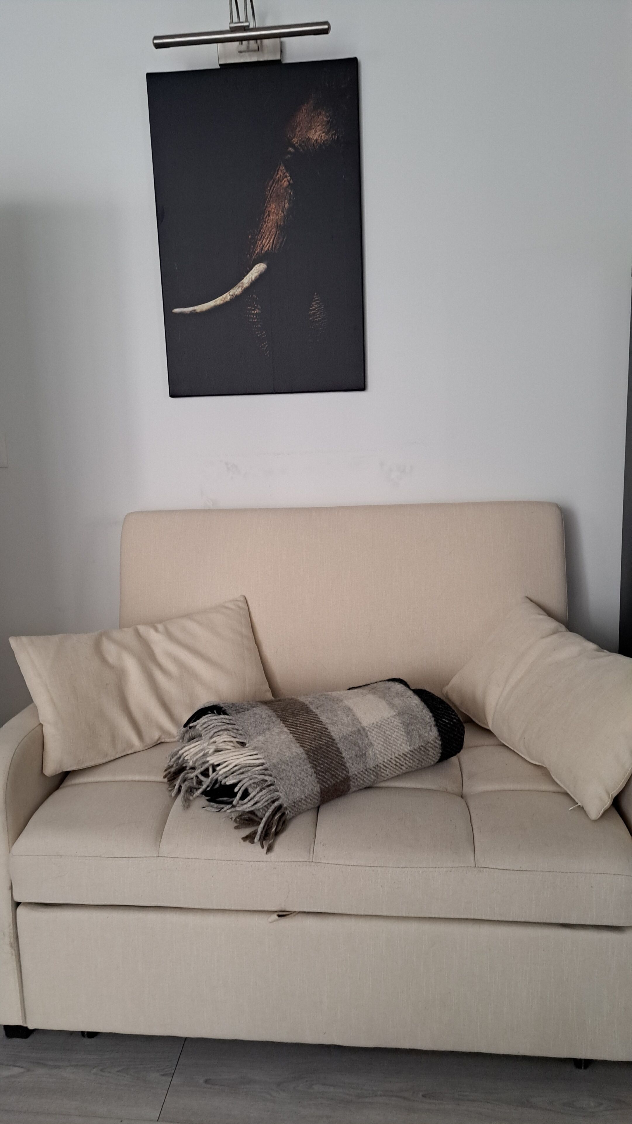 Ein beiges Sofa mit zwei Kissen und einer gestreiften Decke.