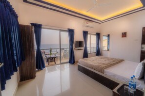 A hotel room with a bed, a TV, a balcony with a table and chairs, and a view of the sea. - 8 BHK VILLA Momentous Villa (Mahabaleshwar)
