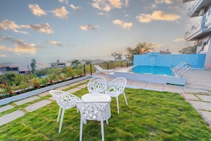 A swimming pool with a blue mosaic border, surrounded by white chairs and a small table. - 8 BHK VILLA Momentous Villa (Mahabaleshwar)