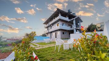 Un immeuble à plusieurs étages doté de balcons, un jardin avec des chaises et un ciel dégagé.