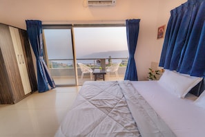 A bedroom with a bed, a view through a glass door, a table with chairs, and a potted plant. - 8 BHK VILLA Momentous Villa (Mahabaleshwar)