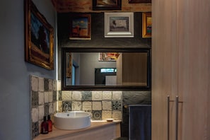 Ein Badezimmer mit einem runden Waschbecken, einer gefliesten Rückwand und einem Spiegel darüber.