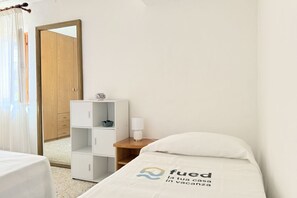 Una camera d'albergo con un letto, un comodino, uno specchio, un armadio e una finestra con tende.