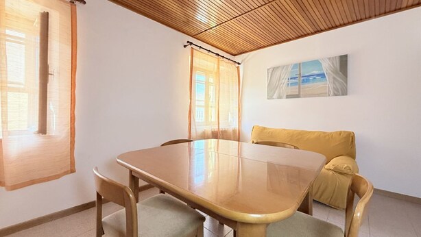Um quarto com teto de madeira, uma mesa de jantar com cadeiras, um sofá e um quadro na parede.