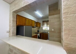 Eine Küche mit weißer Arbeitsplatte, Holzschränken, einem Kühlschrank und einem Fenster mit Jalousien.