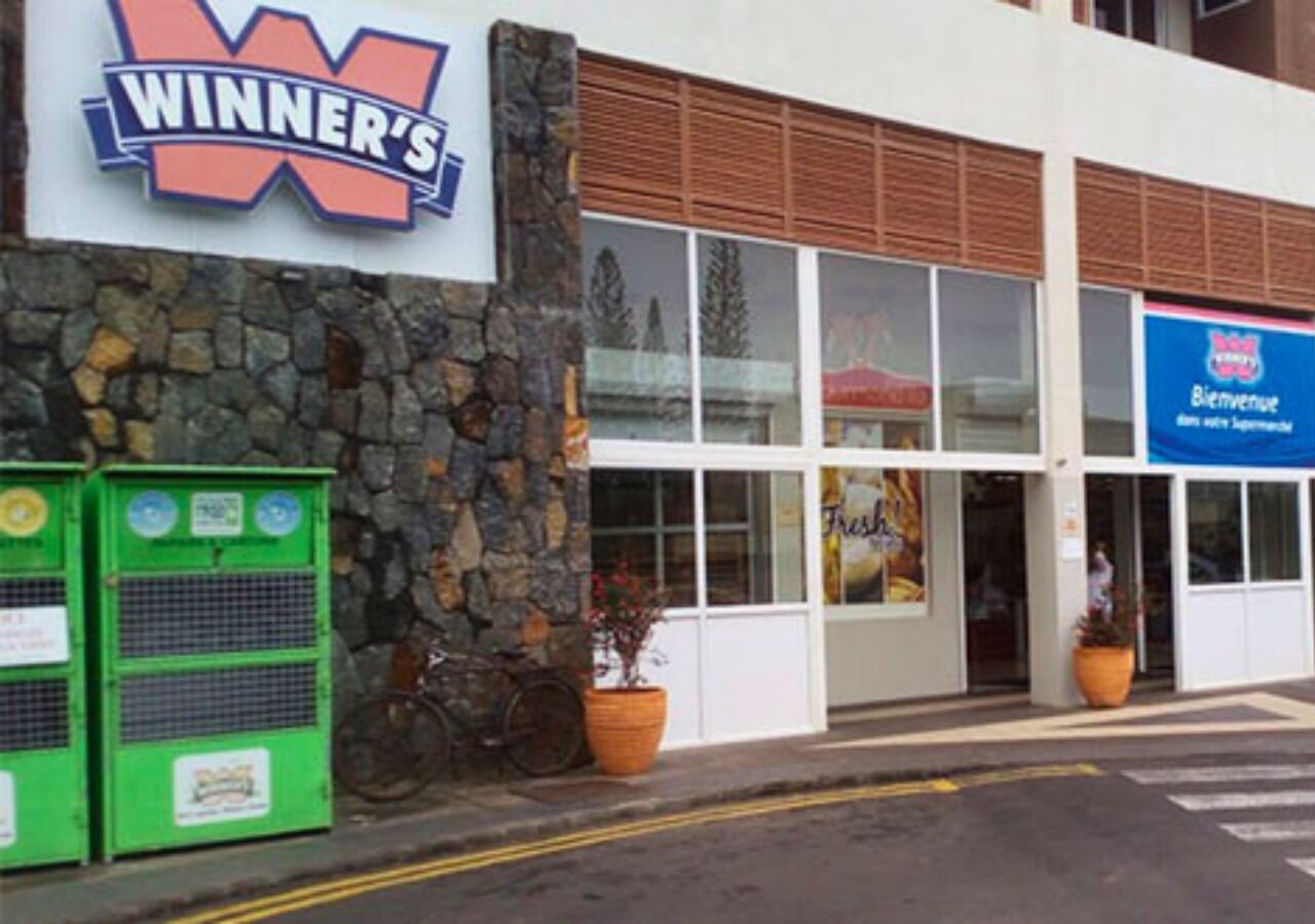 A building with a 'WINNER'S' sign, a storefront with a 'Bieren Sie' sign, and a bicycle parked outside.