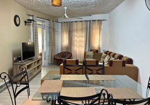 Ein Wohnzimmer mit Esstisch aus Glas, Sofas, Fernseher und Deckenventilator.