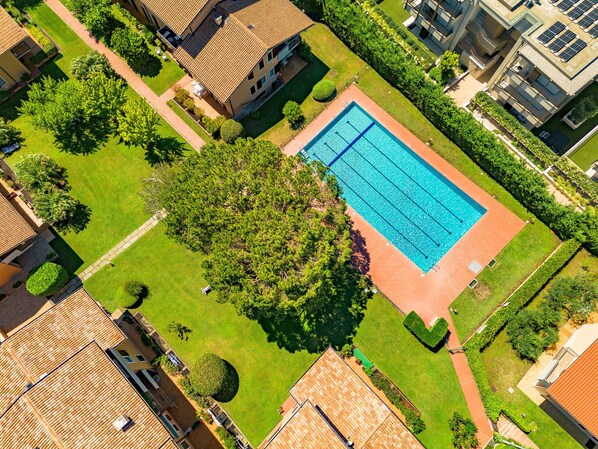 Vista aerea di una zona residenziale con piscina circondata da prati curati e alberi.