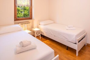 A twin room with two beds, a small table, a lamp, and a window with a view of greenery.