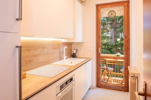Una cocina con armarios blancos, encimera de madera, cafetera y vistas a un balcón con una silla.