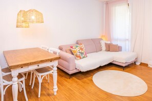 A room with a wooden dining table, white chairs, a pink sofa, a white rug, and a wicker pendant light.