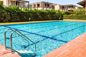 A swimming pool with metal railings, surrounded by a hedge and a building with balconies.