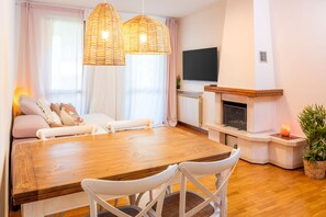 A modern living room with a wooden dining table, white chairs, a fireplace, and a television.