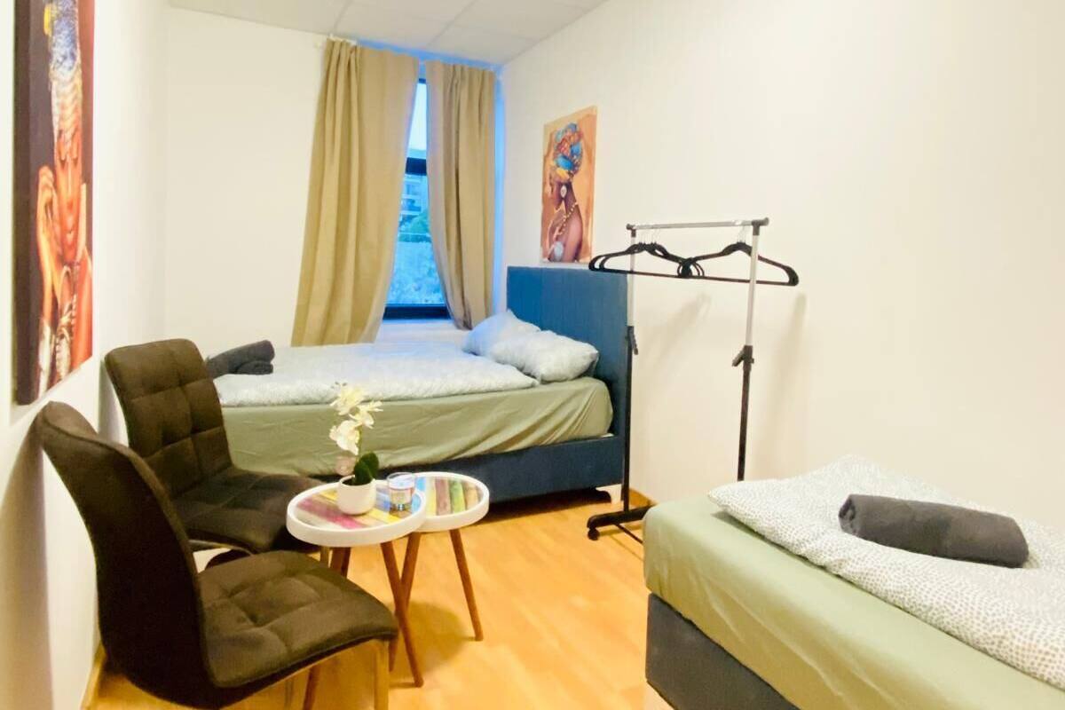 A compact room with a bed, a chair, a small table, and a bedside lamp.