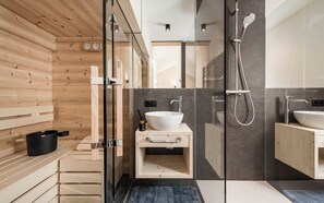 Ein modernes Badezimmer mit einer Holzauna, einer in Glas eingefassten Dusche und einem Waschbecken mit Handtuchhalter.