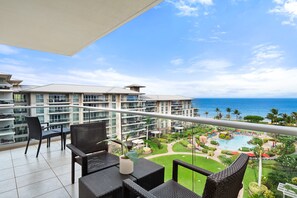 Ein Balkon mit Korbmöbeln, einem Blumentopf und Blick auf ein Resort mit Pool und Palmen.