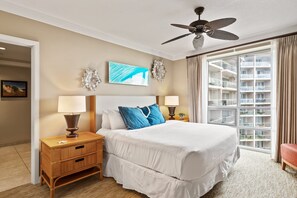 Camera d'albergo con un letto grande, due comodini con lampade, una ventola a soffitto, un'ampia finestra con tende e vista su un edificio.