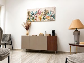 Una sala de estar moderna con un mueble beige, una cafetera, una lámpara y un cuadro abstracto vibrante en la pared.
