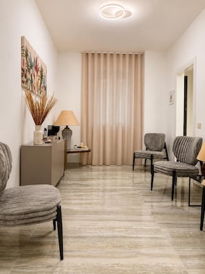 A modern living room with a sofa, armchairs, a coffee table, a lamp, a painting, and a curtain.