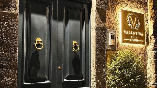 A black double door with a wrought iron gate above it, a sign indicating 'Valentina Rooms' with a three-star rating, and a potted plant to the right. - Valentina Rooms – Elegant Stay in Bronte, Pistacchio e Etna. (Bronte)