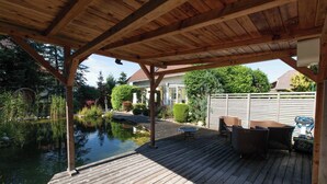 Un patio in legno con uno stagno, mobili da esterno e una zona riparata.
