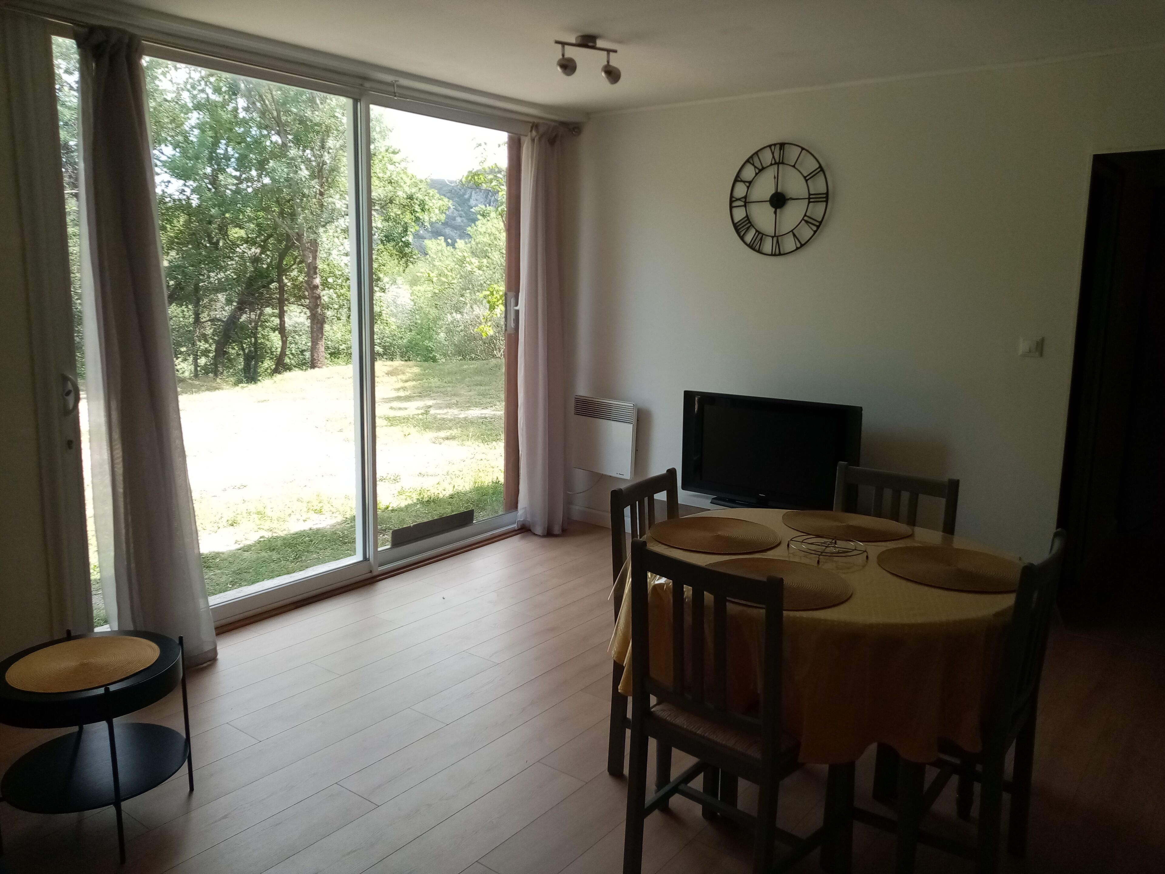 A dining area with a table, chairs, a clock, and a view through a glass door.