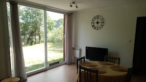 Een eetgedeelte met een tafel, stoelen, een klok en uitzicht door een glazen deur.