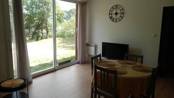 A dining area with a table, chairs, a clock, and a view through a glass door.
