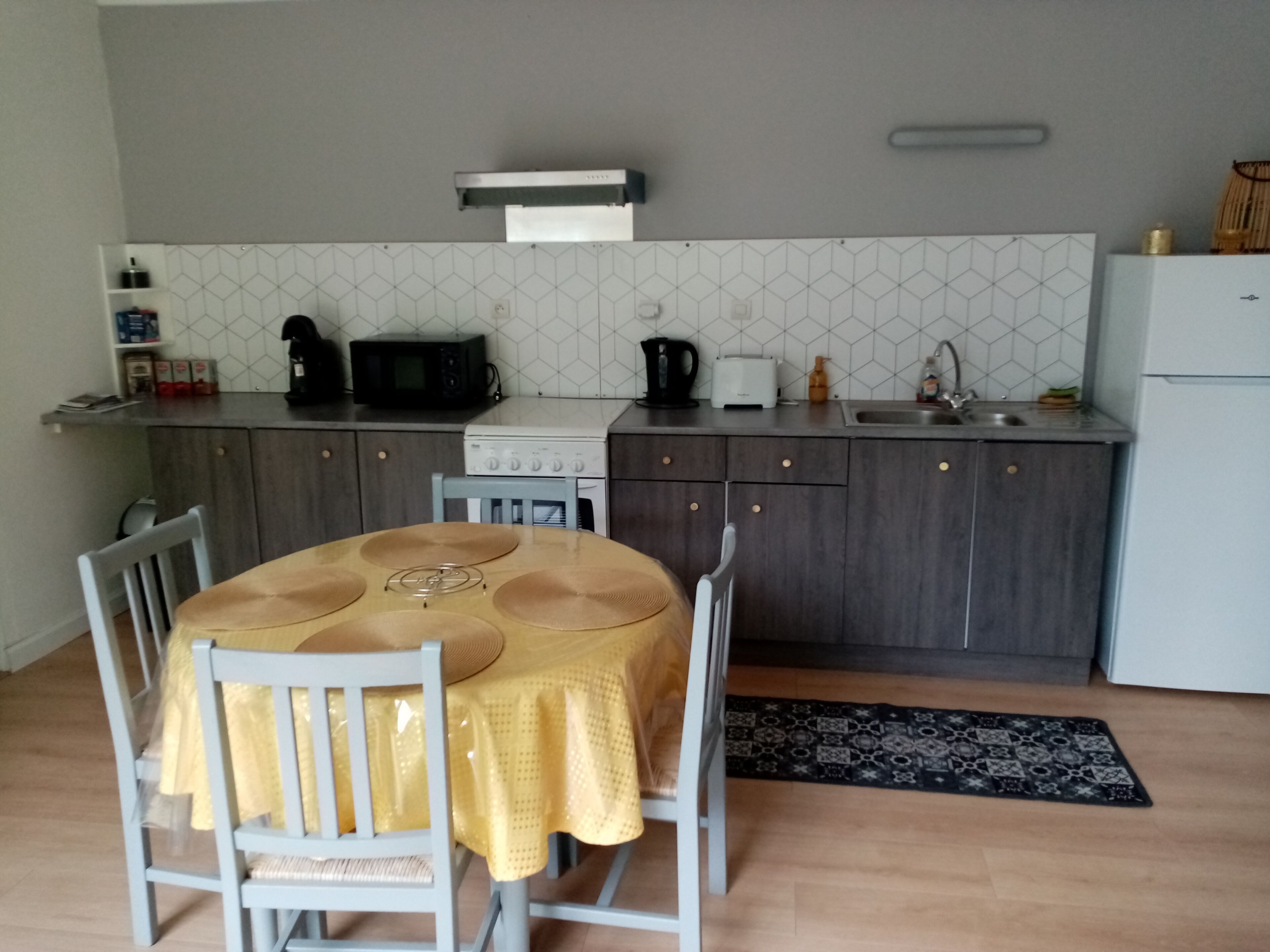 Een compacte keuken met een eettafel, stoelen, een magnetron, een fornuis en een spoelbak.