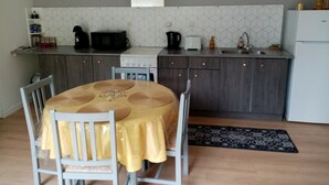 Een compacte keuken met een eettafel, stoelen, een magnetron, een fornuis en een spoelbak.