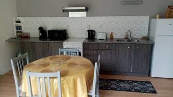 Een compacte keuken met een eettafel, stoelen, een magnetron, een fornuis en een spoelbak.