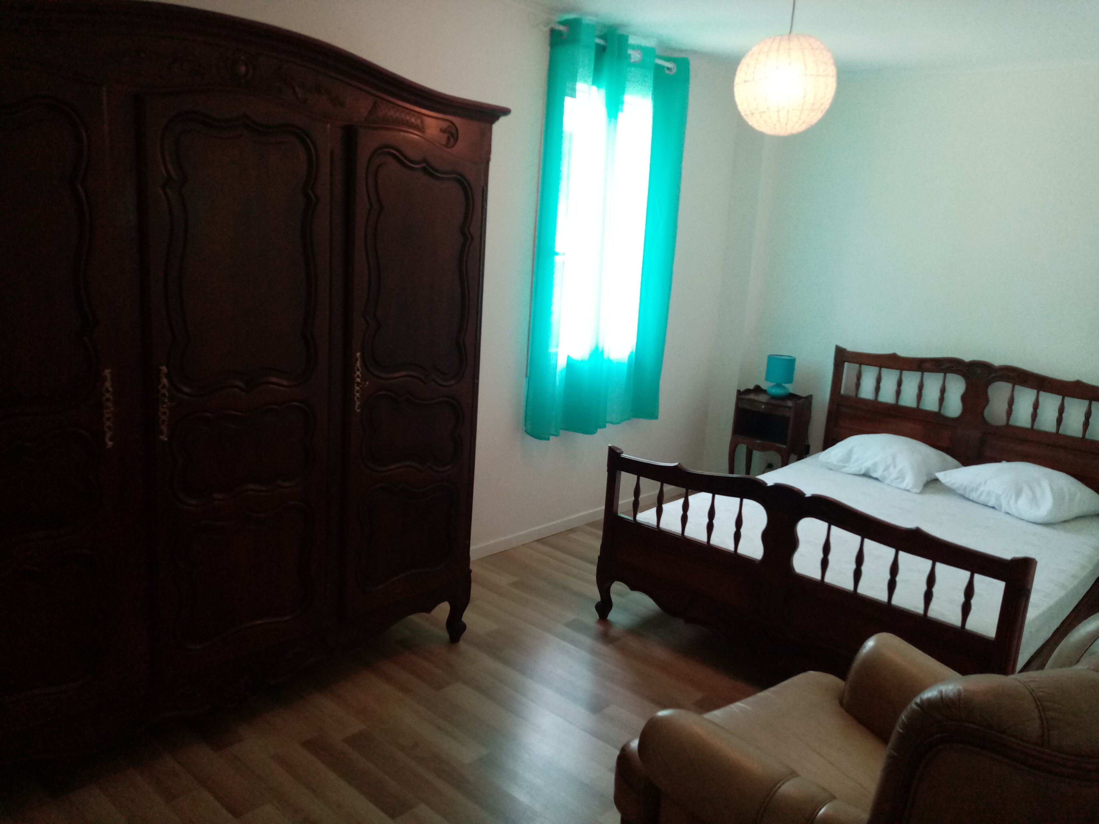 Een slaapkamer met een houten garderobe, een bed met witte lakens, een houten nachtkastje en een hanglamp.