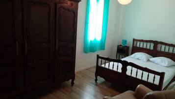 Een slaapkamer met een houten garderobe, een bed met witte lakens, een houten nachtkastje en een hanglamp.