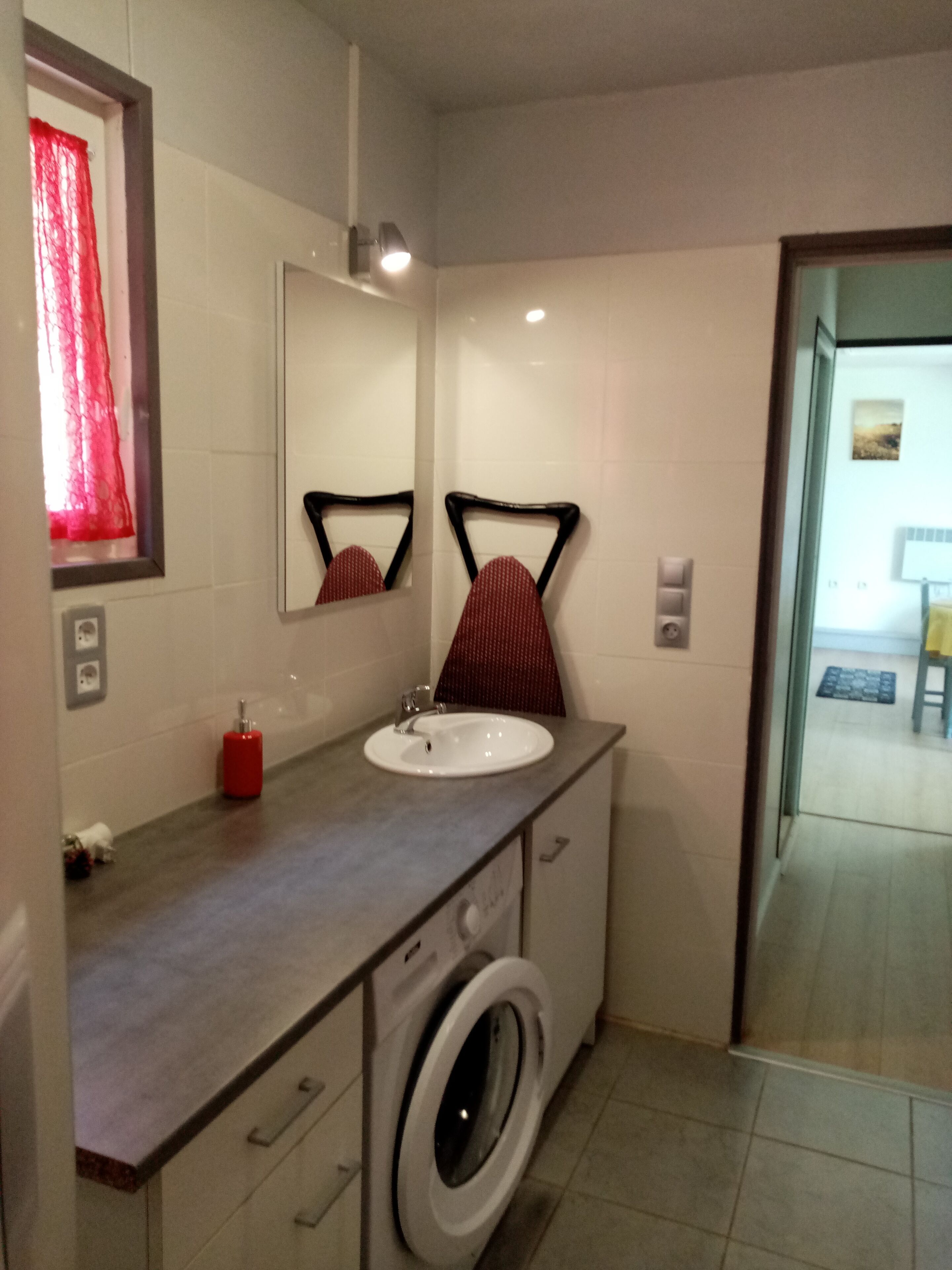 A bathroom with a sink, mirror, red towel, and a washing machine.