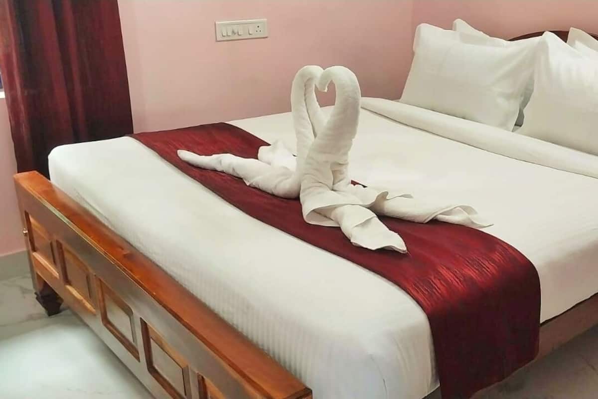 A neatly made bed with a red blanket and white pillows, a wooden headboard, and a small wooden nightstand beside it.