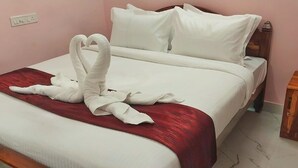 Een net opgemaakt bed met witte lakens en een rode accentkleur, een houten nachtkastje en een stopcontact.