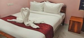 A neatly made bed with white linens and a red accent, a wooden nightstand, and a wall socket.