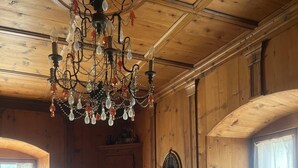 Une pièce chaleureuse aux murs en bois, avec une table ronde, un canapé, un tapis à motifs, un lustre et une fenêtre agrémentée de rideaux.
