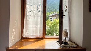 Une pièce avec un banc en bois, une fenêtre avec des rideaux, un radiateur et une vue sur la verdure et un bâtiment.