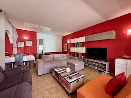 Uma sala de estar com sofá, mesa de centro, televisão e área de jantar com mesa e cadeiras.