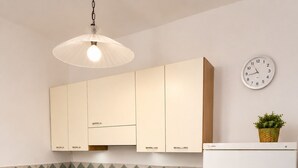 Une cuisine avec des meubles de couleur beige, un micro-ondes noir, un réfrigérateur blanc, une horloge et un luminaire suspendu.