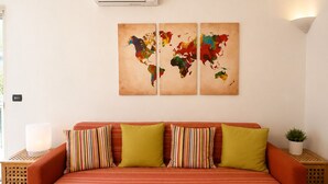 Une pièce comprenant un canapé, une œuvre d’art représentant une carte du monde, un climatiseur et une petite plante.