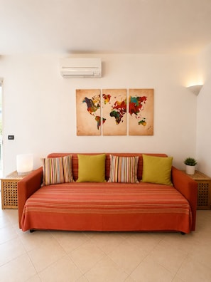 A room with a sofa, a world map artwork, an air conditioner, and a small plant. - SMART EMERALD COAST (provincia della gallura nord-est sardegna)