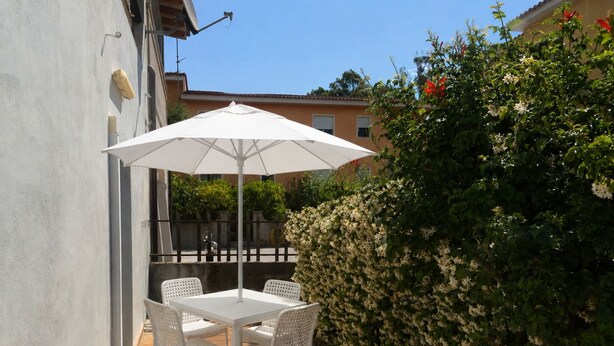Une terrasse avec une table et des chaises blanches, un parasol et une haie.