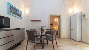 Een kleine keuken met een eettafel, stoelen, een televisie en een koelkast.